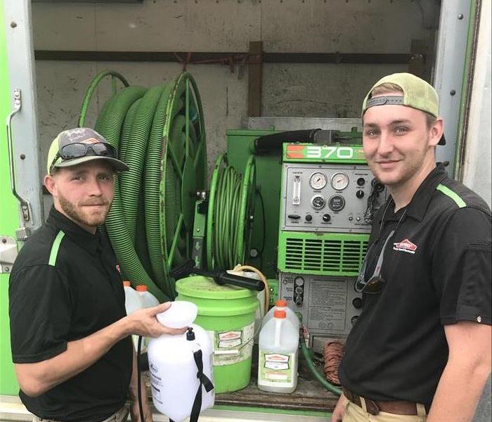 Two SERVPRO employees standing at the door of a stocked SERVPRO vehicle