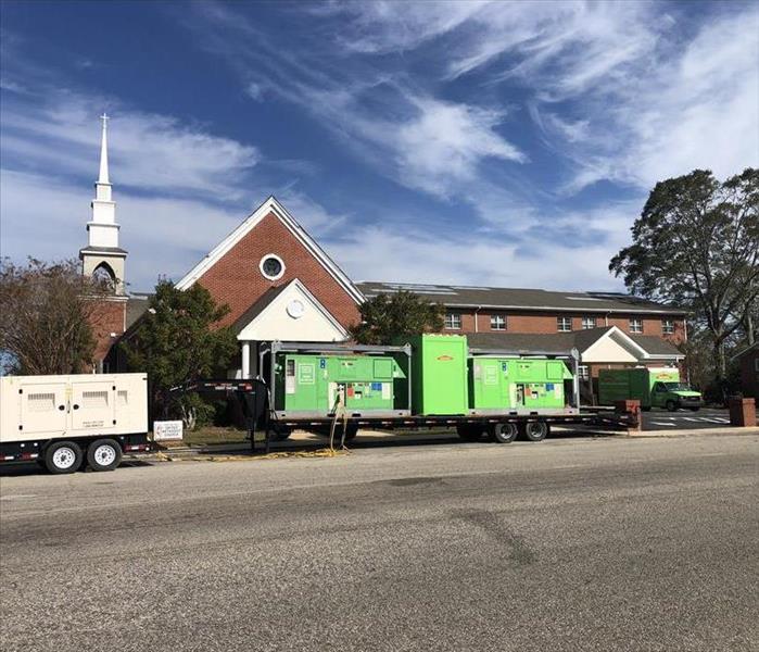 A blue sky with white clouds and green equipment sits in a gray parking lot next to a red brick church.